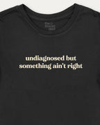 Black t-shirt with white text 'undiagnosed but something ain't right' on a white background